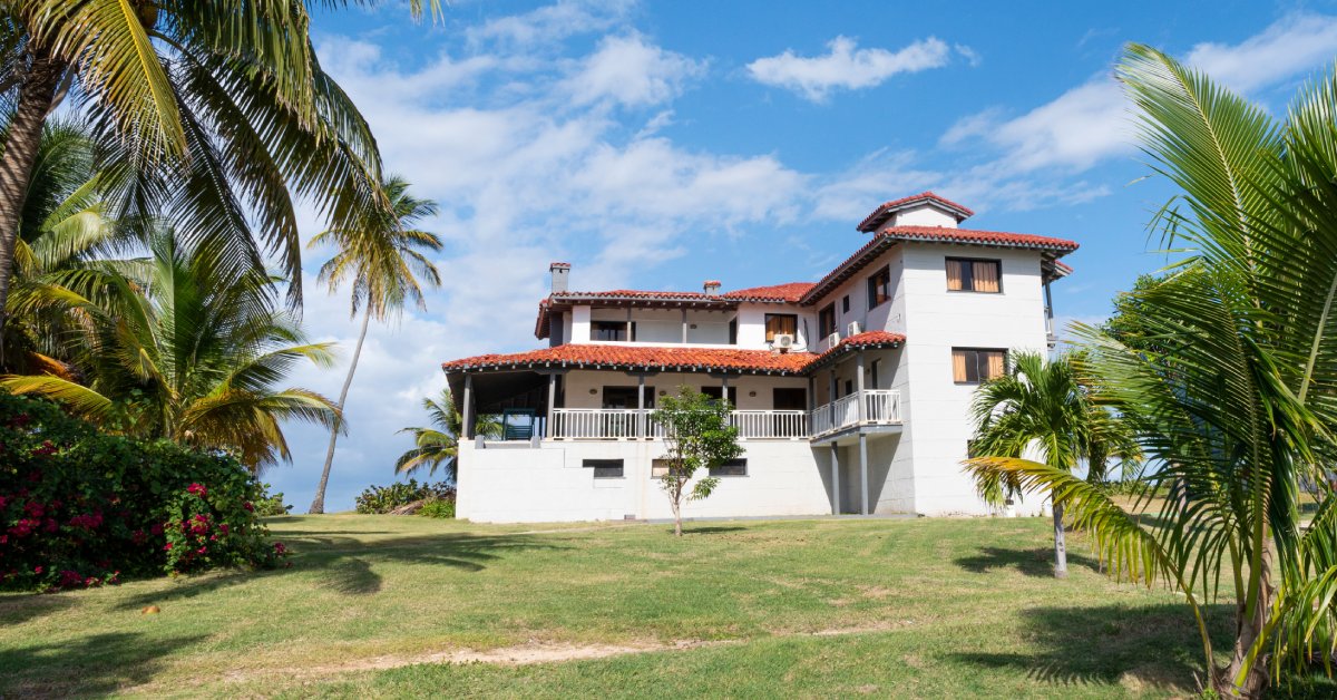 A modern white oceanfront vacation home in the Caribbean sits under a clear blue sky on a bright sunny day.